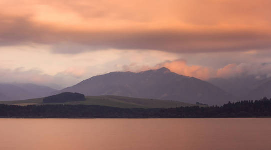 长曝光拍摄的Liptovska马拉湖，低塔特拉斯山脉和多云的天空在日落。