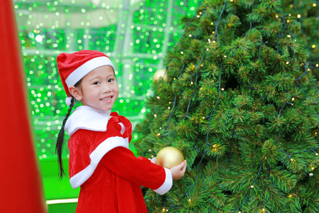 快乐可爱的亚洲小女孩圣诞老人服装附近的圣诞树和背景。圣诞节寒假概念..