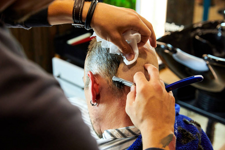 直边在理发店用直边剃须刀在理发店用木制纹理剃光的年轻秃头男子的