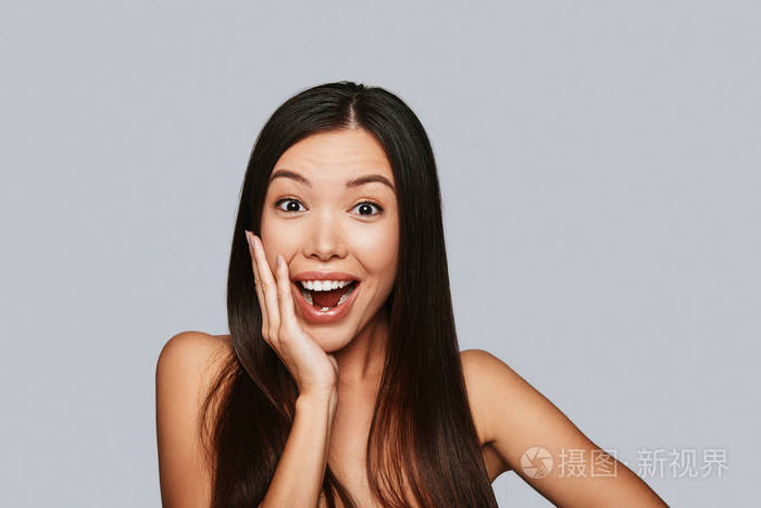 令人惊讶的年轻亚洲女人张开嘴双手捂着脸看着镜头