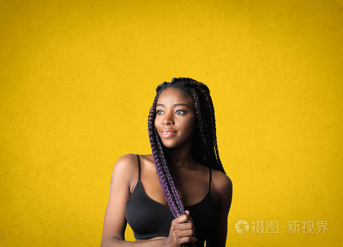 穿着黑色t恤站在黄色墙边的漂亮年轻黑人女子