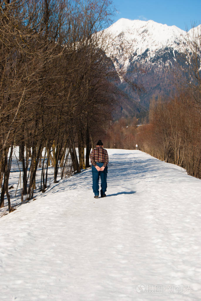 老人在一个阳光明媚温暖的日子里走在雪地里山景尽收眼底