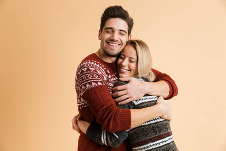 快乐的年轻情侣穿着毛衣拥抱在米色背景上的形象。