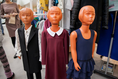 红色销售标志在儿童服装店橱窗旁边的一个穿着冬衣的人体模型.