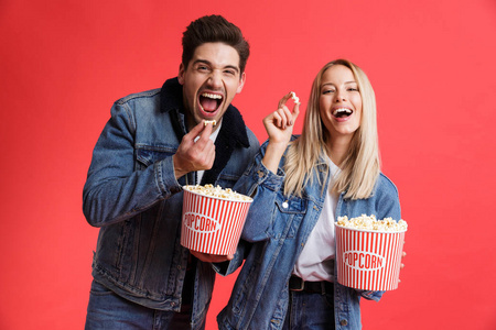 一对穿着牛仔夹克的年轻夫妇站在一起，在红色背景下观看电影吃爆米花