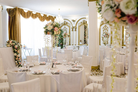 在装饰有鲜花的餐厅为客人准备的婚礼桌。 白色桌布，水晶眼镜和餐具，没有人。