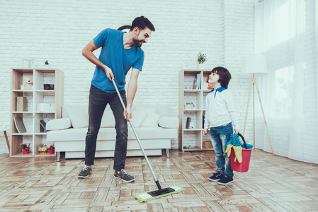 男人花时间和他的儿子在一起。 男孩的父亲从事抚养孩子的工作。 父亲正在教儿子打扫卫生。 父子用拖把洗地板。 人们位于卧室里。