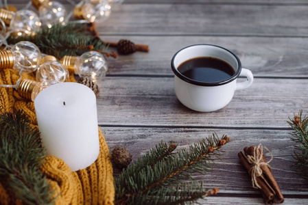 一杯咖啡蜡烛肉桂云杉枝和温暖的橙色围巾，并在木桌上用LED灯装饰。 冬季概念。 平躺顶部视图。