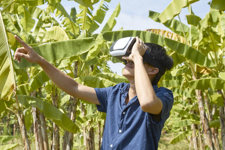 亚洲男人喜欢虚拟现实坐在户外公园的草地上。 VR耳机眼镜设备。 大自然的户外背景。 人与技术概念