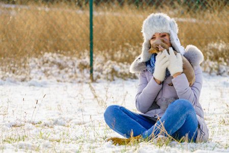 年轻的女人在冬天玩得很开心。 白雪皑皑的白雪中，一只小纯种狗在玩