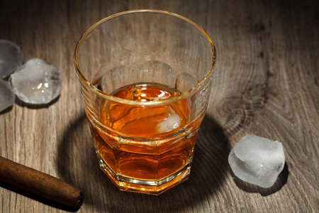 一杯含冰块的酒精饮料和一张木桌上的雪茄。 玻璃杯里的威士忌