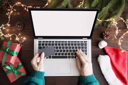 圣诞节销售。妇女用信用卡购物的笔记本电脑。屏幕上文本的空间。在键盘上的顶视图, 人的手, 在木桌上的圣诞礼物。假期理念