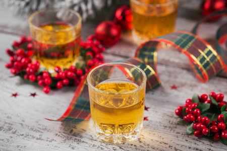 威士忌白兰地或白酒酒和白色木制背景上的圣诞装饰品。 季节性假日概念。
