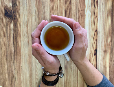 s hands holding a cup of hot tea. The background is wooden table