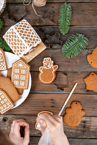 一个年轻的女孩装饰姜饼干的形式雪人圣诞节早晨。女人在蜂蜜姜饼上画冰。木棕色的桌子。复制空间