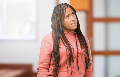 一位戴着辫子的年轻黑人妇女的肖像怀疑和困惑地思考一个想法或担心某件事