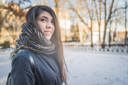 东部女孩看上去冬天在公园里散步。 穿着带围巾的冬天夹克的女人。 街头服装