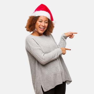 年轻的黑人妇女戴着圣诞老人的帽子，手指指向一边