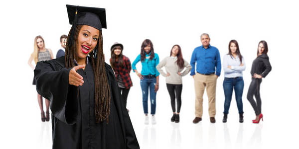 年轻的毕业黑人妇女戴着辫子，伸出手来问候某人，或打手势帮助快乐和兴奋