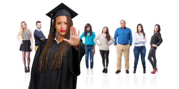 年轻毕业的黑人妇女戴着辫子，严肃而坚定地把手放在前面，停止手势否认概念