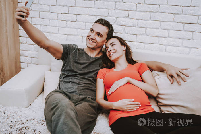 情侣正在手机上自拍. 夫妻是男人和孕妇. 女孩在摸她的肚子.