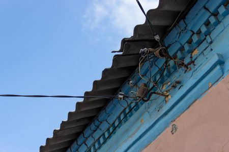 旧房子石板屋顶下绝缘子上的基本电线。 天空和粉红色，砖墙上有蓝色的石膏。 乌克兰DNipro市2018年11月
