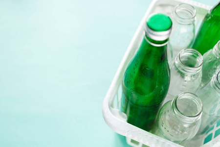 不同的玻璃瓶废物准备在绿色背景下的白色篮子中回收。 社会责任生态护理再循环家庭观念