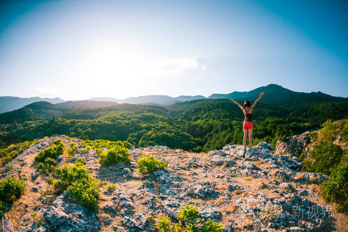山顶上的女孩举起双手那个女人爬上了山顶享受着她的成功夕阳的光芒