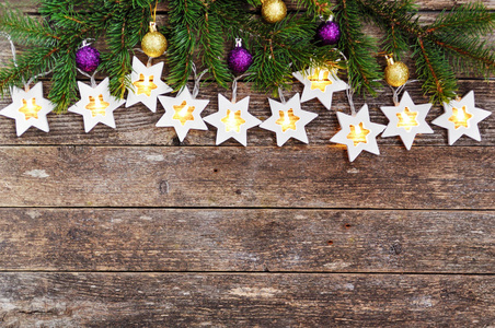圣诞节边界舒适的温暖灯光，花环，星星和冷杉树枝，装饰着金色和紫色的球在乡村的木制背景上。 上面的风景。 手一伸。 复制空间