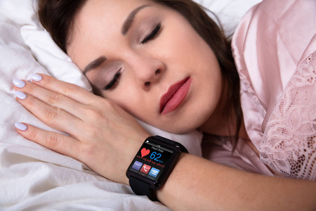 睡在床上的漂亮女人用智能手表显示心跳率