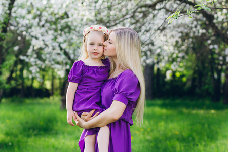 年轻漂亮的女人带着一个小女儿穿过盛开的苹果园。 家庭休息和爱的概念。 调色。