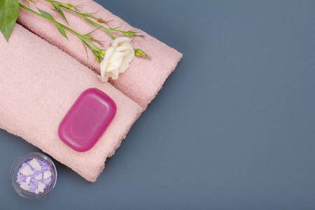 用于面部和身体护理的水疗产品。 天然海盐肥皂和粉红色毛巾与花在灰色背景。 水疗和身体护理概念。 上面的风景。