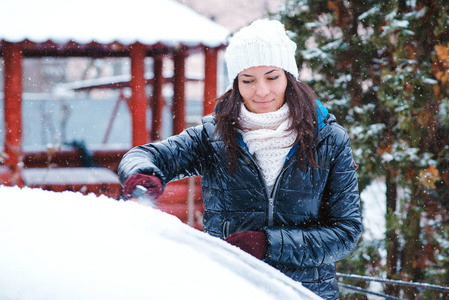 女人把雪从车里移走。 男人用刷子把雪从汽车挡风玻璃上清理出来。 下雪的冬天天气。 暴风雪后雪中的汽车。 冬季天气和车辆概念