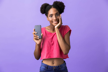 令人惊讶的非裔美国妇女微笑着拿着手机在紫色背景下被隔离的照片