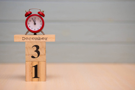 12月31日设置在木制日历和红色闹钟与蓝色背景. 钟展5分钟到午夜照片