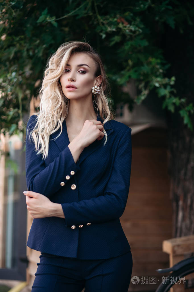 优雅的金发碧眼的女人在深蓝色西装与黄金按钮