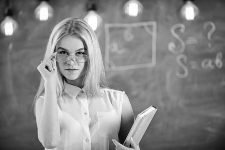 学生, 老师看起来自信的眼镜, 站在教室, 黑板上的背景, 弥散。有吸引力的讲师概念。有书的女人准备上课, 凝视观众