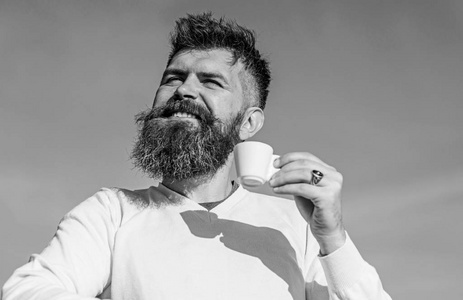 长胡子的人喜欢喝咖啡。男人用胡子和胡子在笑脸上喝咖啡, 蓝天背景, 弥散。有胡子的男人用咖啡杯喝咖啡咖啡品酒师概念