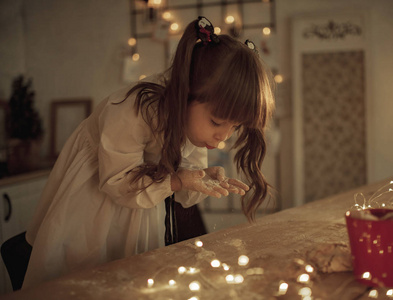 小女孩把面粉撒在桌子上，然后用灯泡在花环的背景上吹着她那脏兮兮的手。