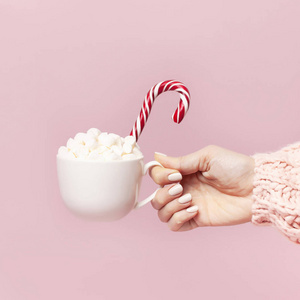 女手穿着针织毛衣，手拿着一杯棉花糖和圣诞节糖果在粉红色背景平躺复制空间冬季传统食品节日装饰庆祝圣诞节。