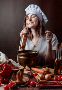年轻漂亮的女孩穿着厨师制服和小瓶橄榄油。各种香料和草药的香橄榄油