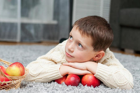 拿着苹果的男孩躺在家里的地毯上