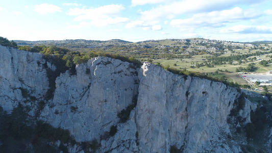 游客在山间深渊的顶部景色。拍摄。迷人的岩石悬崖景色和绿色植被全景。一群勇敢的游客在悬崖上休息, 反对蓝色多云的天空