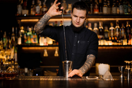 鸡尾酒摇床酒保把一杯鸡尾酒从瓶子里倒入酒吧柜台上的钢制摇床照片