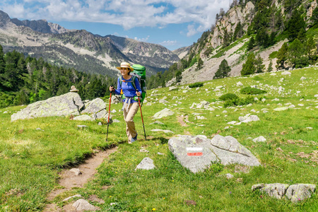 年轻女子带着背包和徒步旅行杆在山上徒步旅行。 山径路线概念