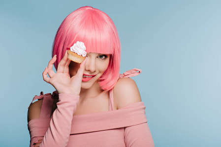 迷人的微笑女孩，戴着粉红色假发，抱着蓝色的纸杯蛋糕