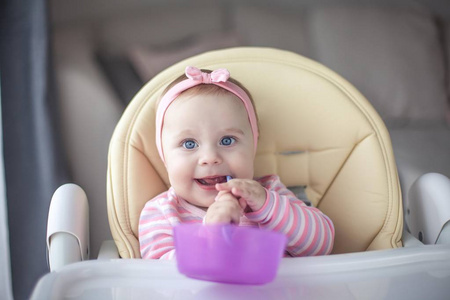 s chair and holds a spoon. Portrait of a baby with blue eyes in 