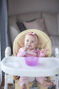 s chair and holds a spoon. Portrait of a baby with blue eyes in 