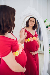 美丽的孕妇在明亮的房间的镜子