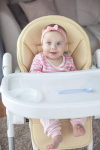 s chair and holds a spoon. Portrait of a baby with blue eyes in 